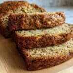 Moist zucchini bread slices with a golden crust on a wooden cutting board. Freshly baked, featuring green zucchini and nuts for a tasty, healthy snack or breakfast treat.