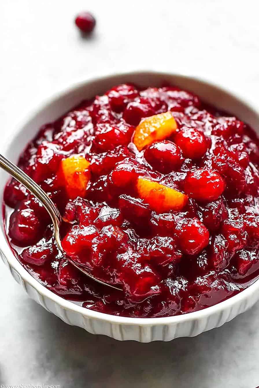 Sweet tart cranberry-orange jam in a white bowl with a spoon, ready to serve as a holiday topping or spread.