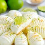 Lime-flavored creamy desserts on a white plate with lime slices and whole limes in the background, garnished with lime zest and crumbs.