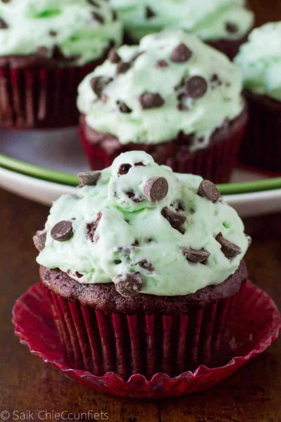 Rich chocolate cupcake with mint frosting topped with chocolate chips, in a red cupcake liner, served on a wooden surface. Perfect for desserts, baking, and chocolate lovers.