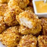 Crispy chicken nuggets with almond coating and dipping sauce on a white plate, close-up shot.