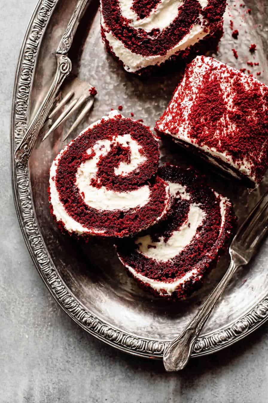 Red velvet cake rolls with cream cheese filling on vintage silver tray, decorated with red sprinkles, perfect for celebration desserts and baking recipes.