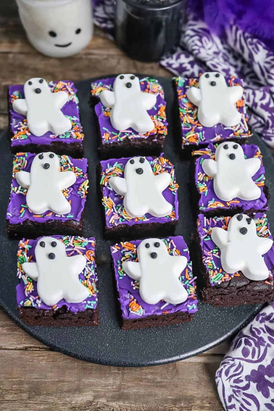 Colorful Halloween ghost brownies with purple frosting and sprinkles on black serving platter. Perfect for spooky treats and festive gatherings.
